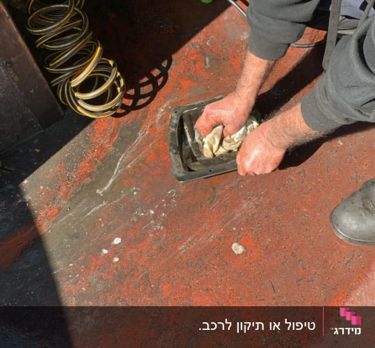 אדם מנקה חלק מתכת עם מטלית על רצפה אדומה